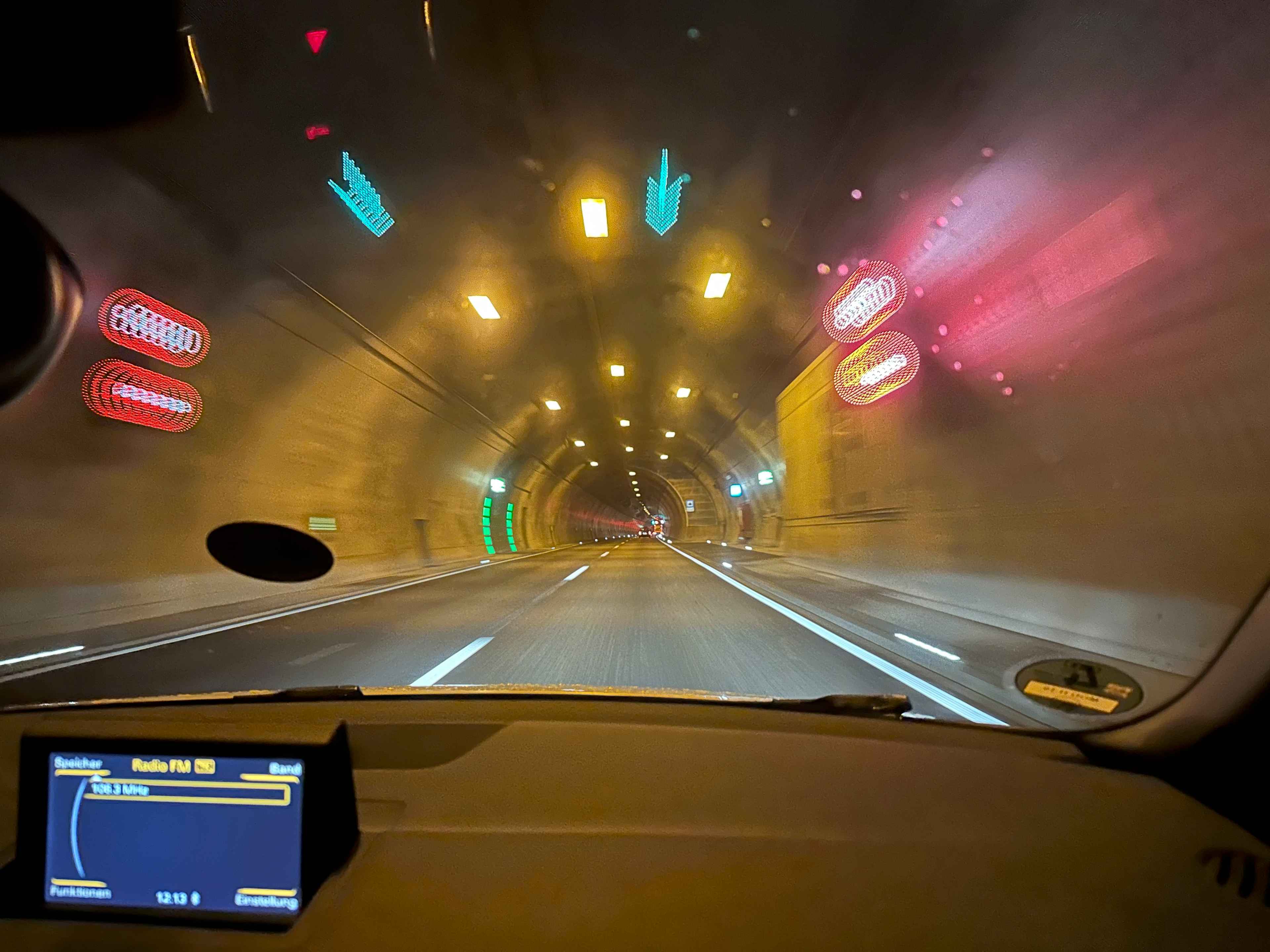 Blick aus einem Auto während der Durchfahrt durch einen Tunnel mit rot und grün reflektierenden Verkehrsanzeigen.