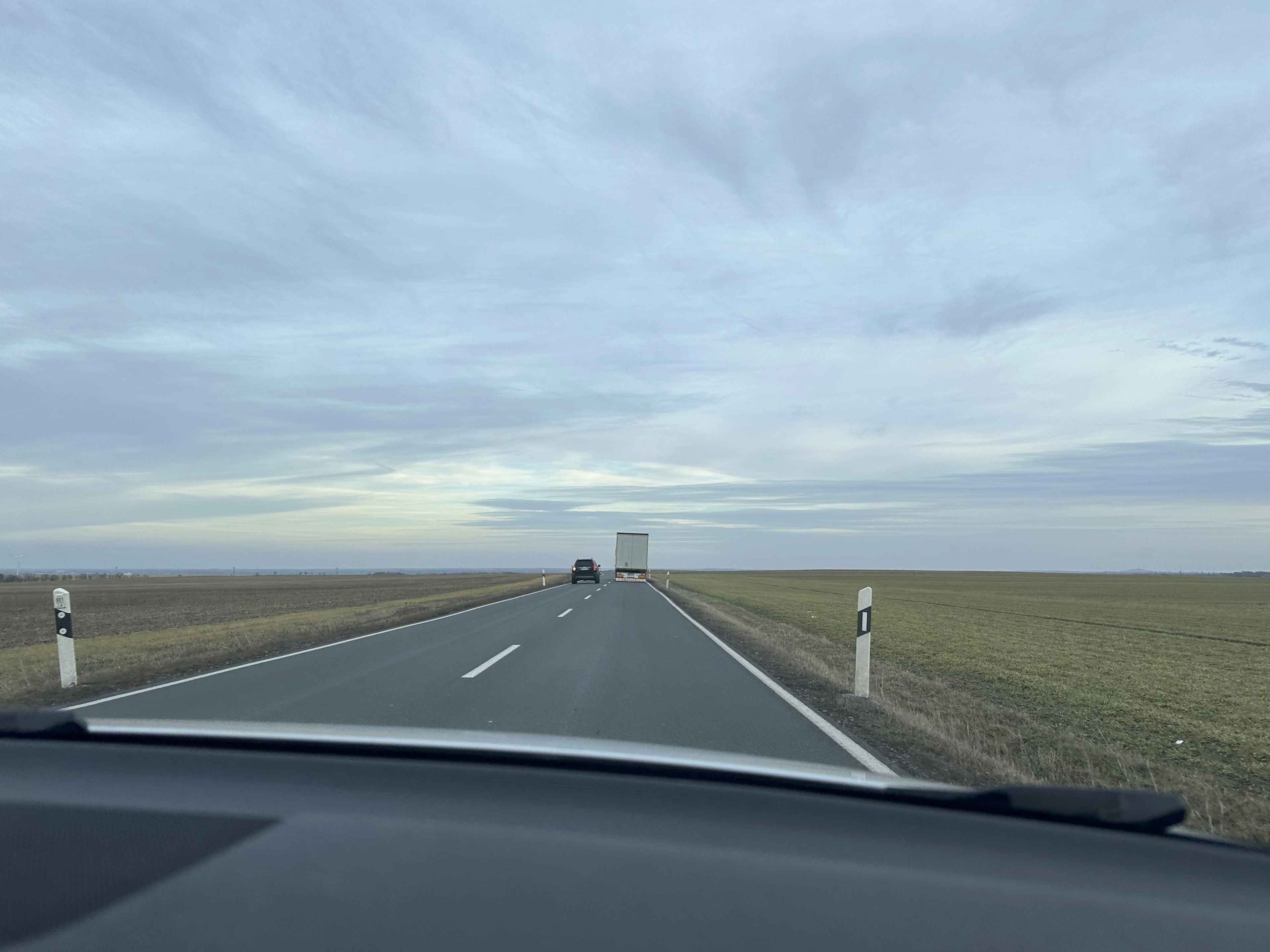 Blick aus einem Auto auf eine gerade, offene Landstraße, die durch flaches, weites Feldland führt.