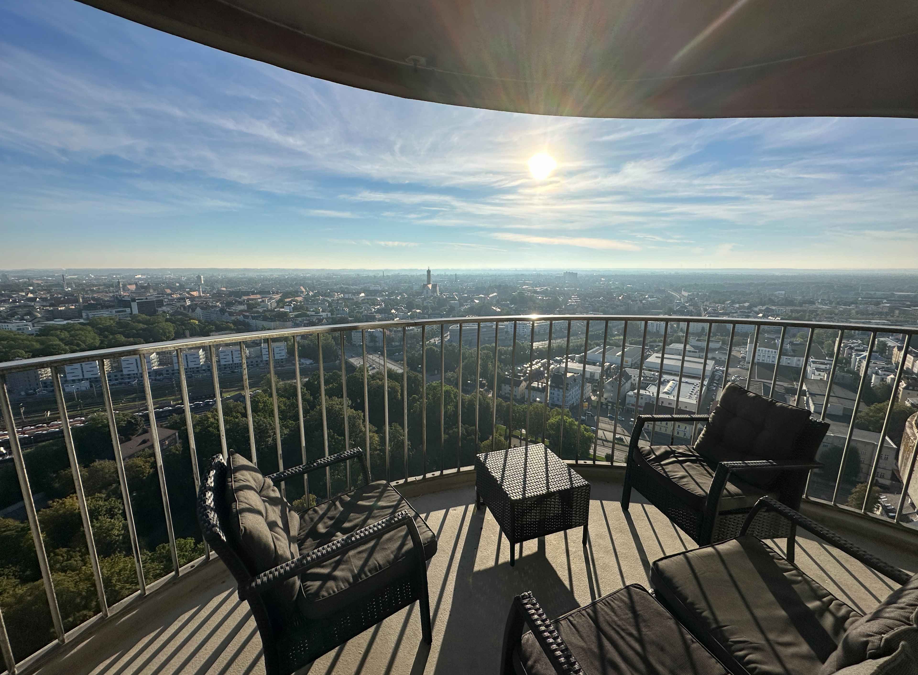 Runder Balkon im Hotelturm mit schwarzen Balkonmöbeln. Im Hintergrund das sonnendurchflutete Stadt-Panorama.