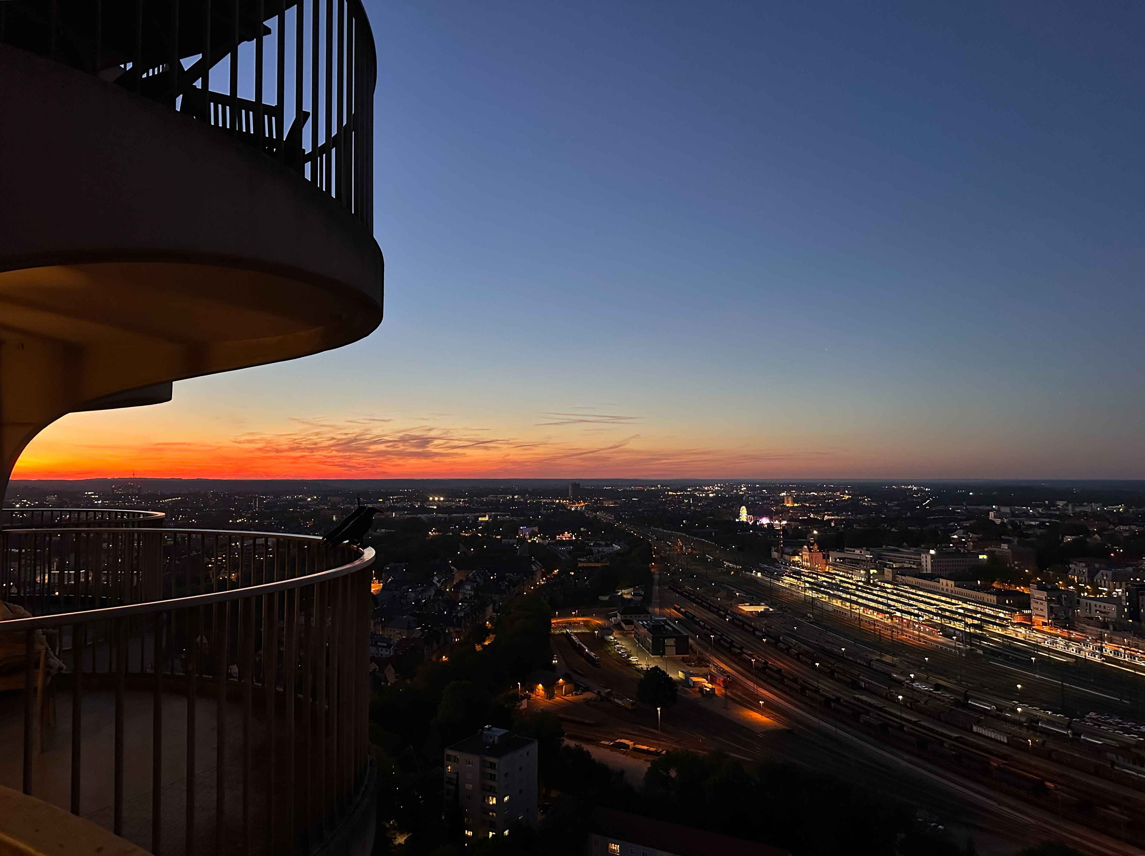 Blick vom Balkon des Hotelturms auf das nächtliche Panorama der Stadt mit beleuchtetem Bahnhof und weiter hinten Riesenrad.
