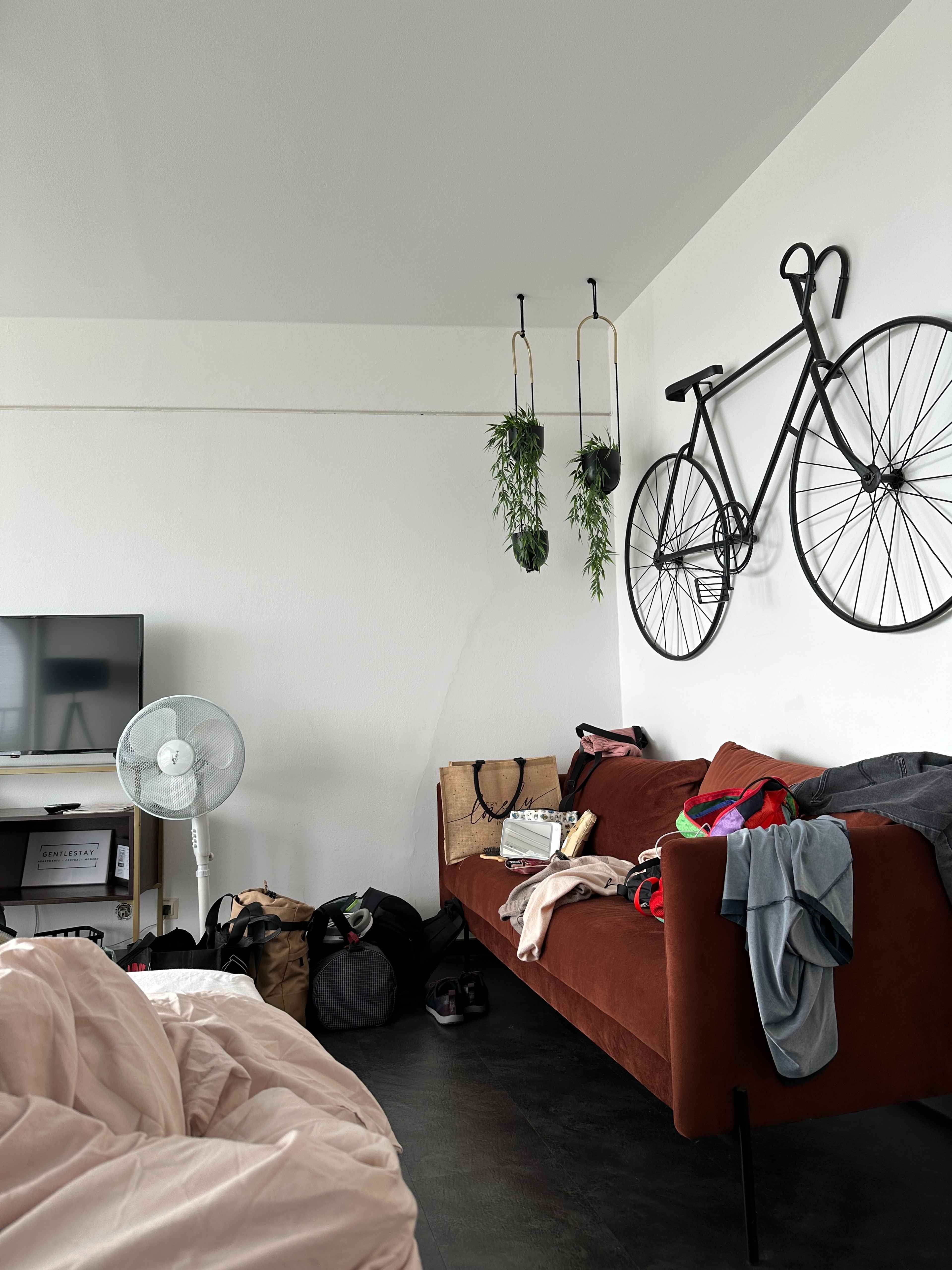Eine rostrote Couch mit verstreut liegender Kleidung in der Ferienwohnung im Hotelturm. Ein Fahrrad als Deko an der Wand.