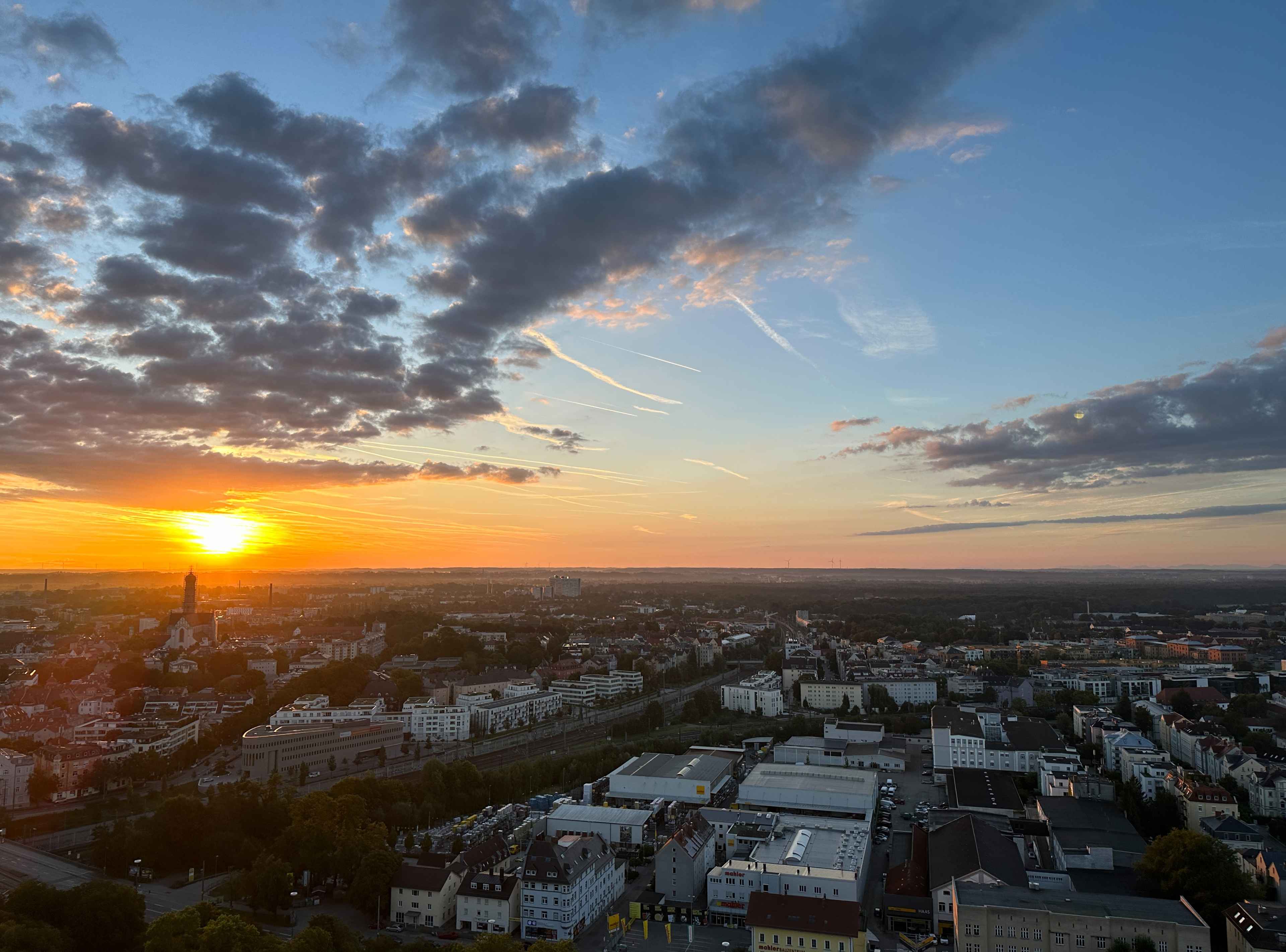 Panoramaaussicht auf Augsburg mit aufgehender Sonne. Horizont in Orange und Blau. Links die kleine Silhouette des Doms.