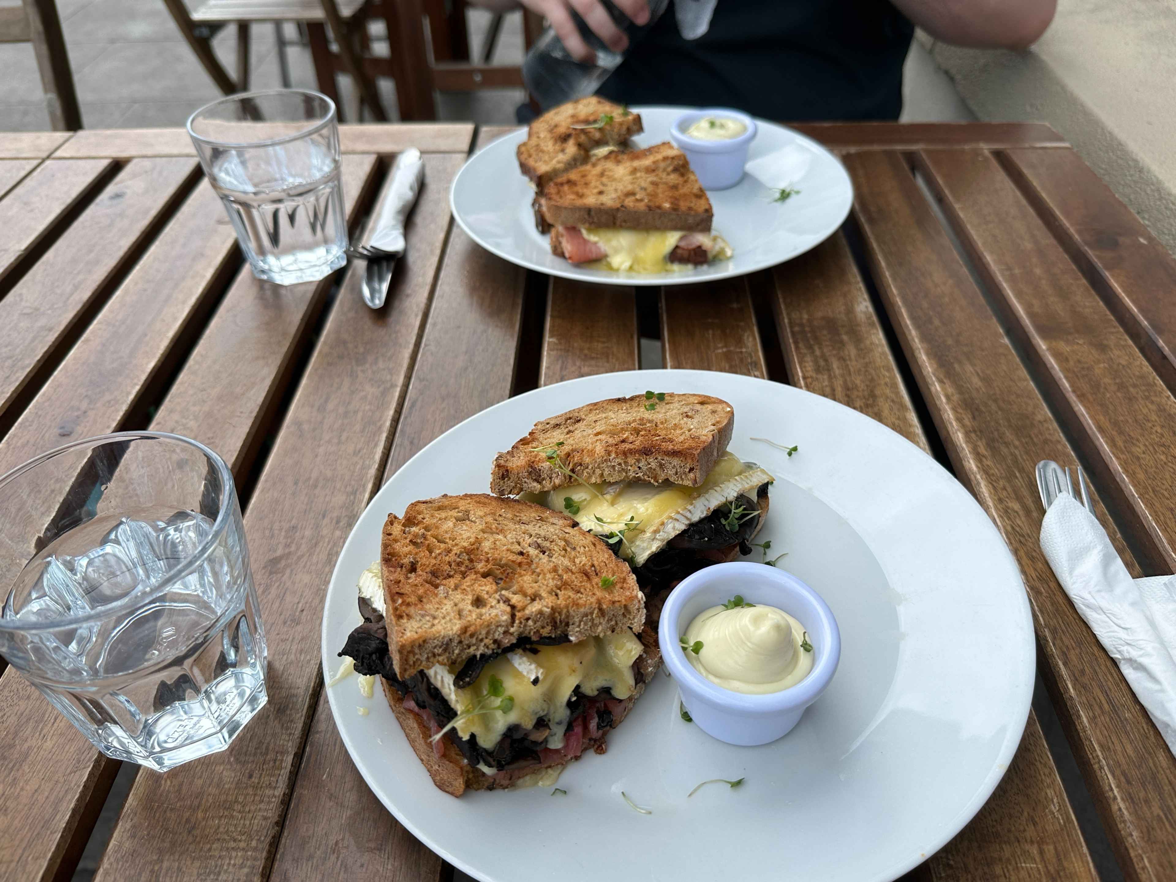 Nahaufnahme von zwei Tellern mit krossen Sandwich-Brotscheiben gefüllt mit schmelzendem Käse auf einem braunen Holztisch.