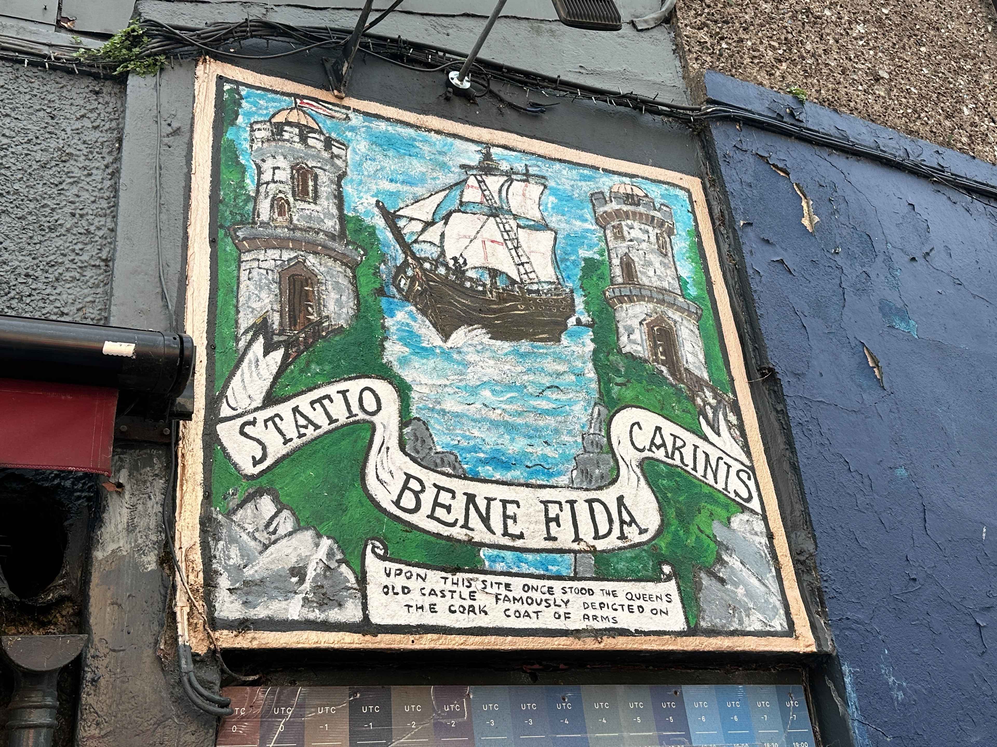 Gemaltes Coat of Arms der Stadt Cork auf einer Wand mit Schiff, Steintürmen und dem Banner "Station Bene Fida Carinis"