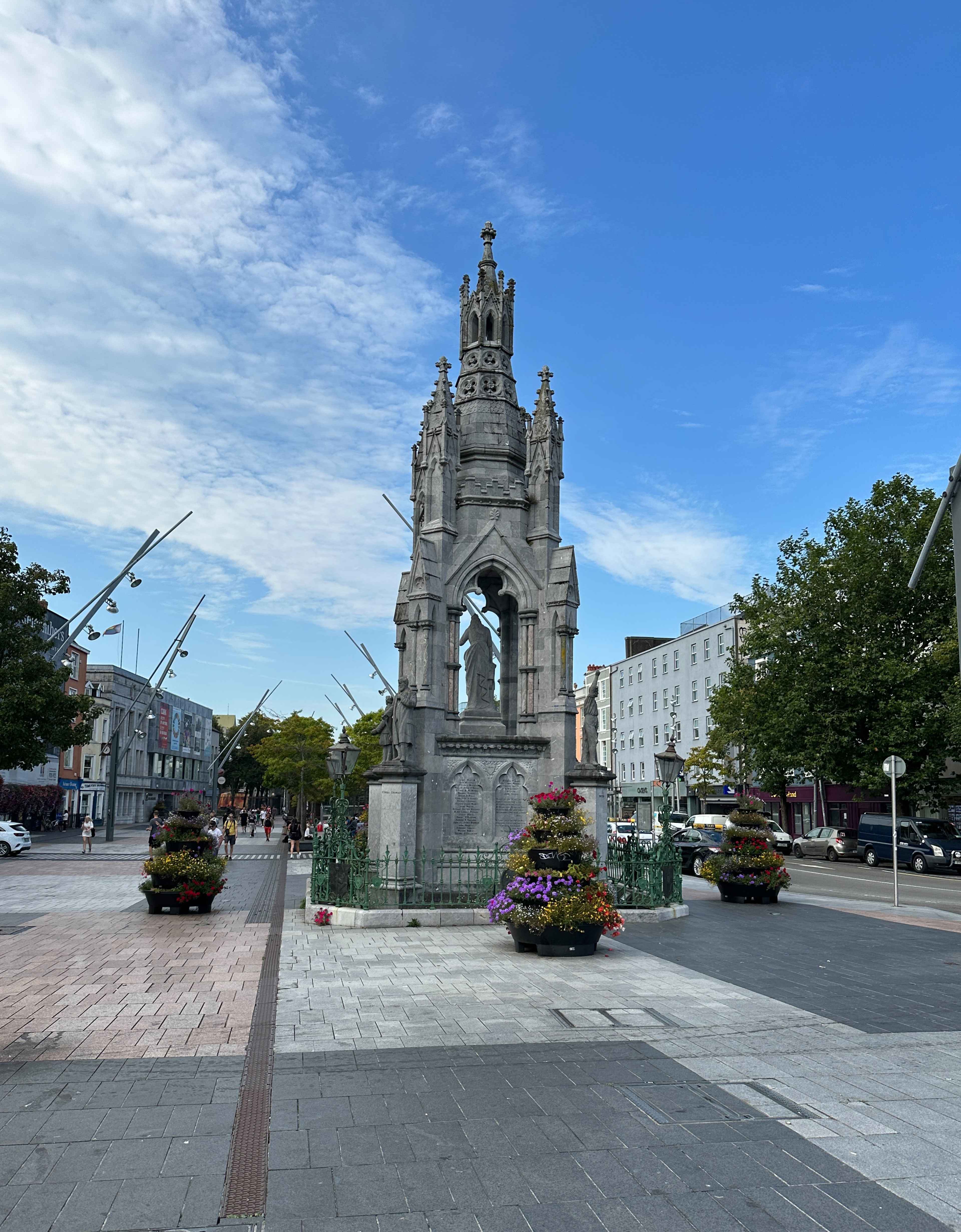 Blick auf das National Monument in Cork mit großen Blumentöpfen an allen Seiten auf einem großen Platz.