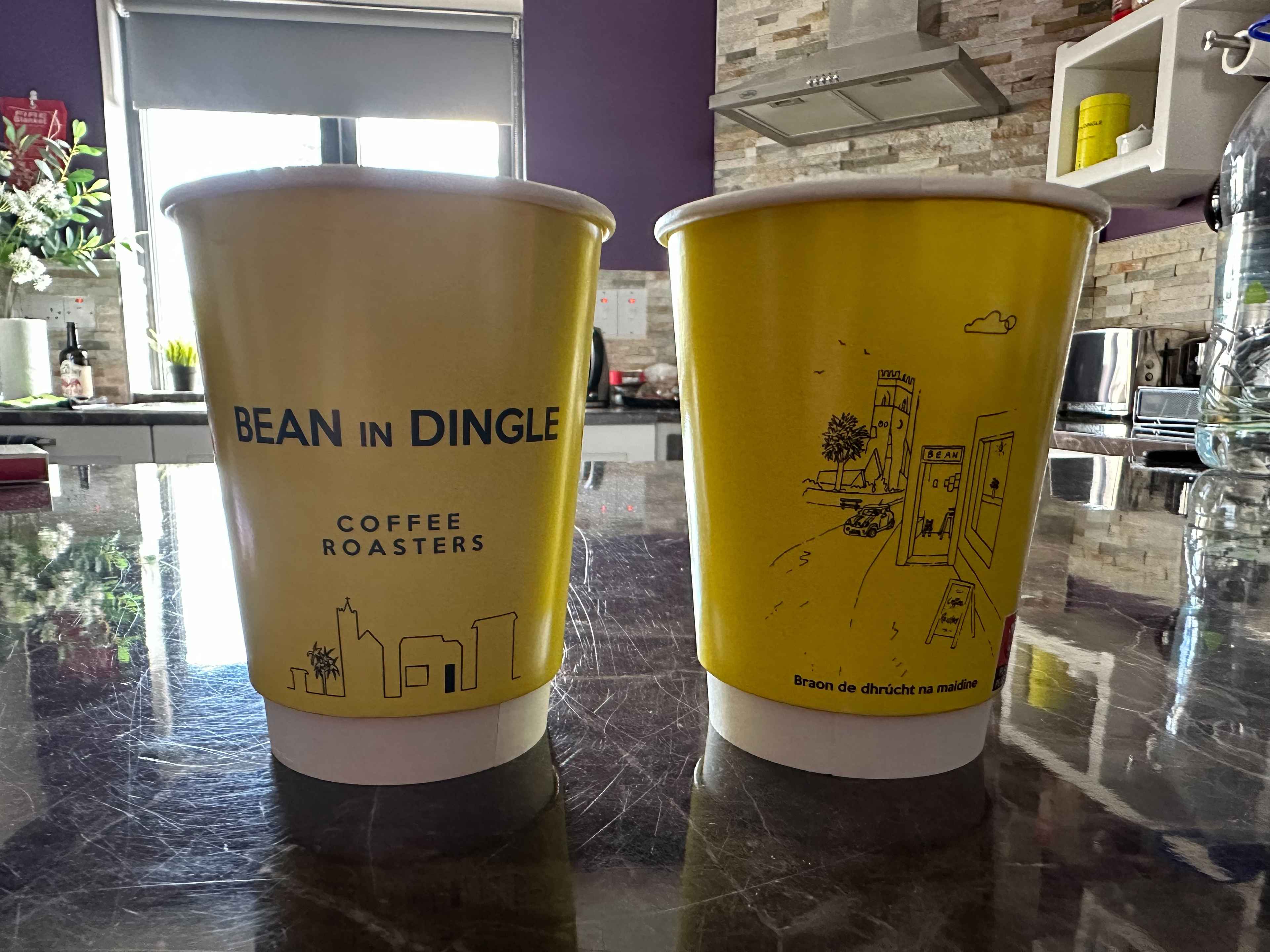 Zwei knallgelbe Pappbecher auf einem schwarzen Küchentresen mit Aufschrift „Bean in Dingle – Coffee Roasters“.