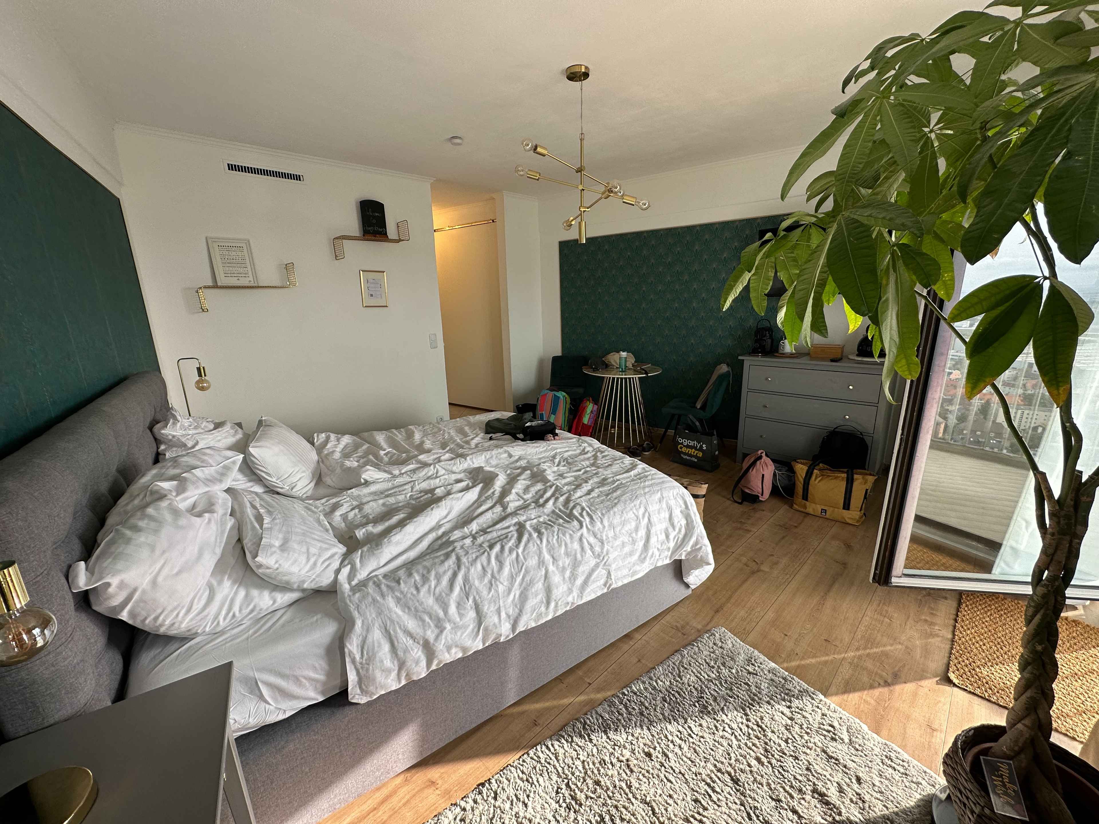 Zimmer der Ferienwohnung im Hotelturm mit Bett mit weißen Lacken im Vordergrund, grünen Wänden und Taschen im Hintergrund.