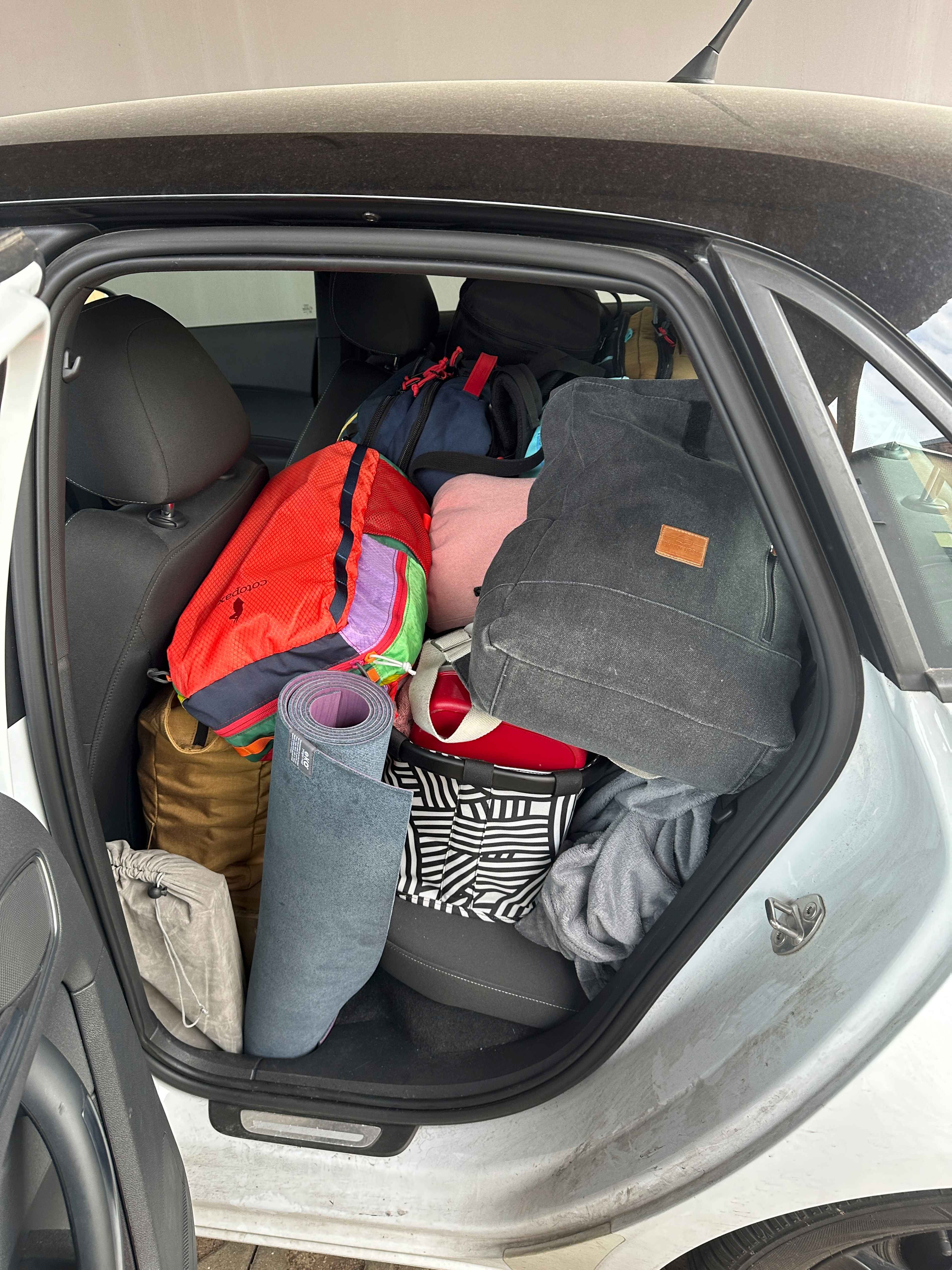 Seitlicher Blick durch die offene Tür eines Autos auf die Rückbank, vollgepackt mit bunten Taschen, Koffern und Rucksäcken.