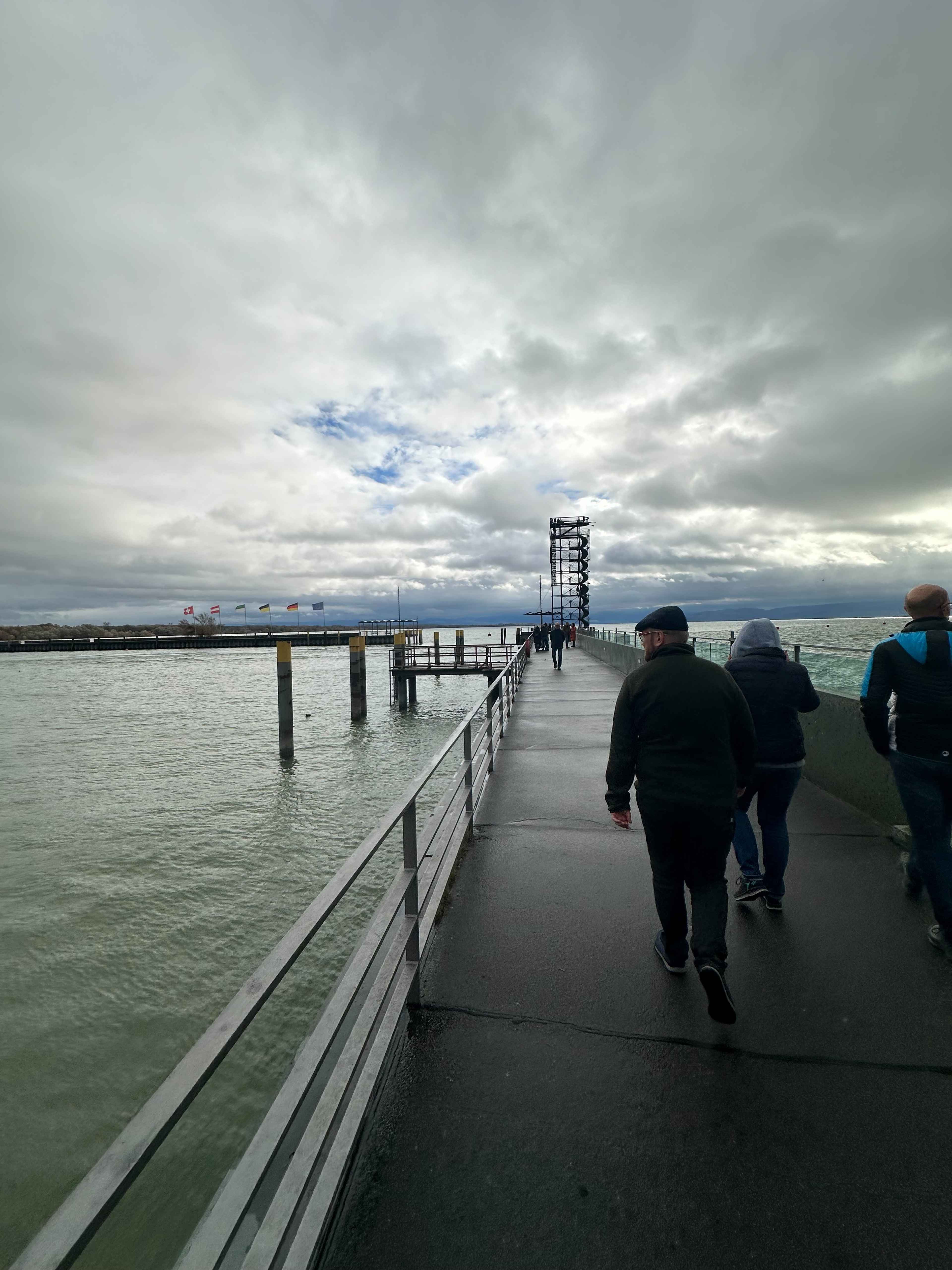 Ein Steg mit Passanten, der über den Bodensee verläuft. Im Hintergrund klein der Moleturm .
