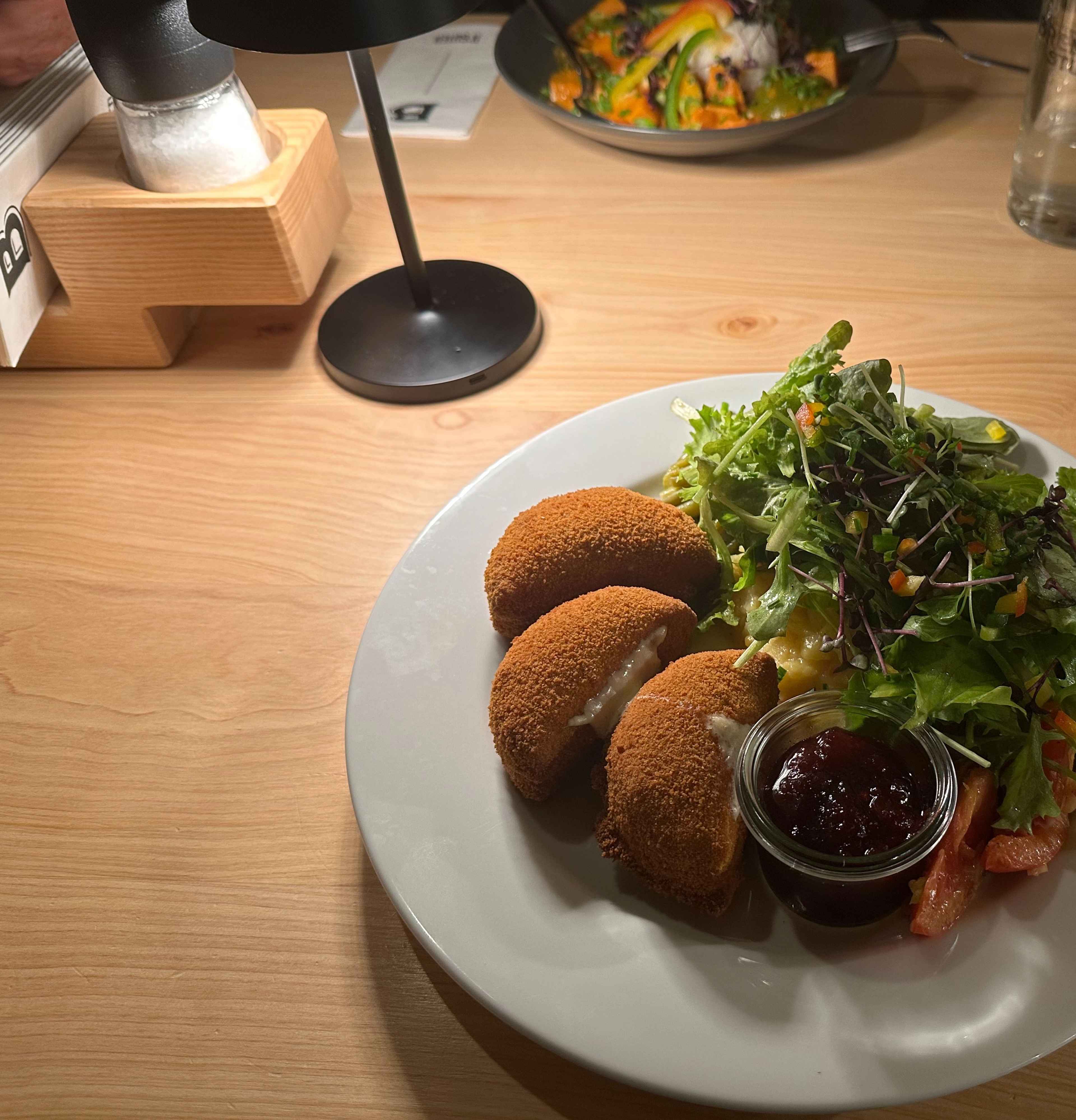 Ein Teller mit paniertem Camembert, Salat und Preiselbeeren, angerichtet auf einem Holztisch im Hintergrund.