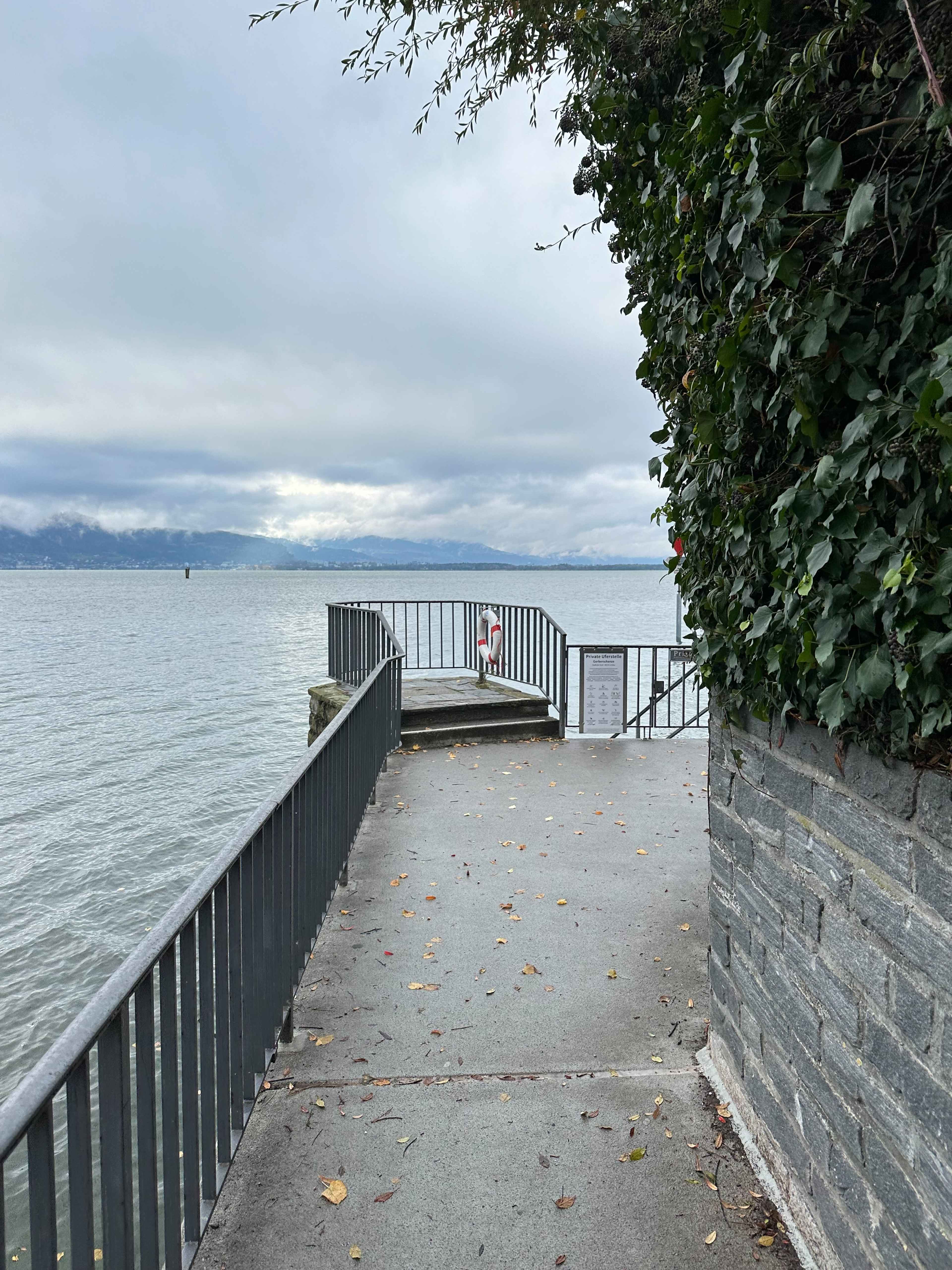 Eine kleine Aussichtsplattform aus Metall ragt über den See, umgeben von Efeu und einer Steinmauer.
