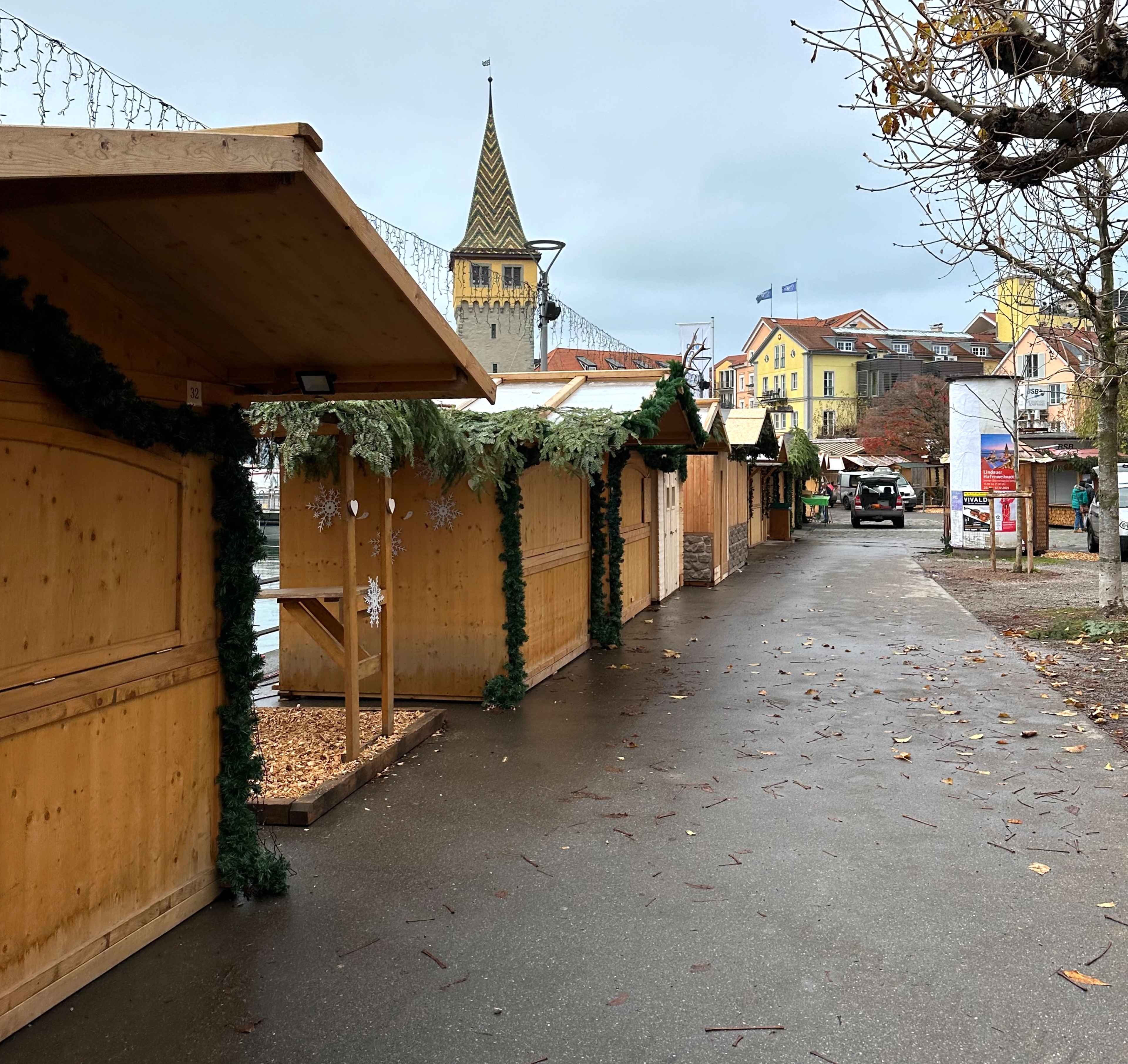 Eine weihnachtliche Marktgasse mit dekorierten Holzhütten und dem Turm des Mangenturms im Hintergrund.