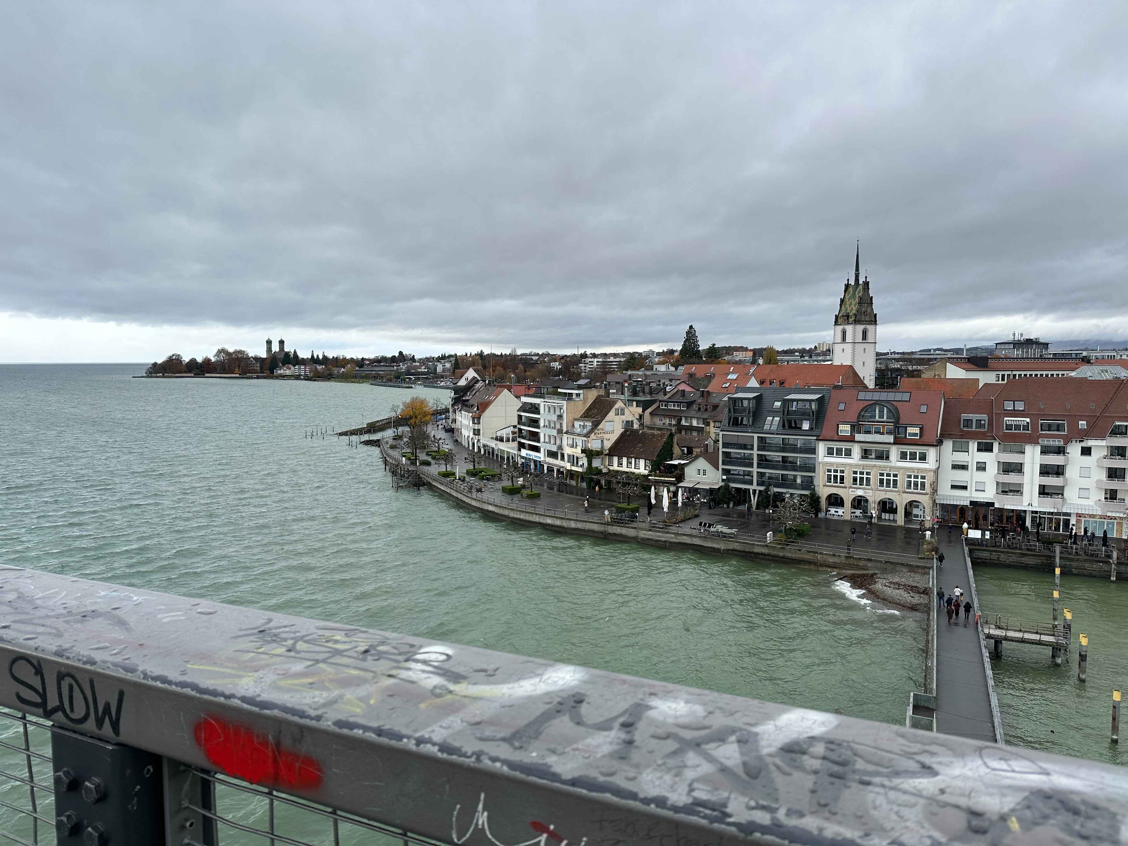 Blick vom Moleturm auf Friedrichshafen mit historischen Gebäuden und einer Promenade am See unter einem grauen Himmel