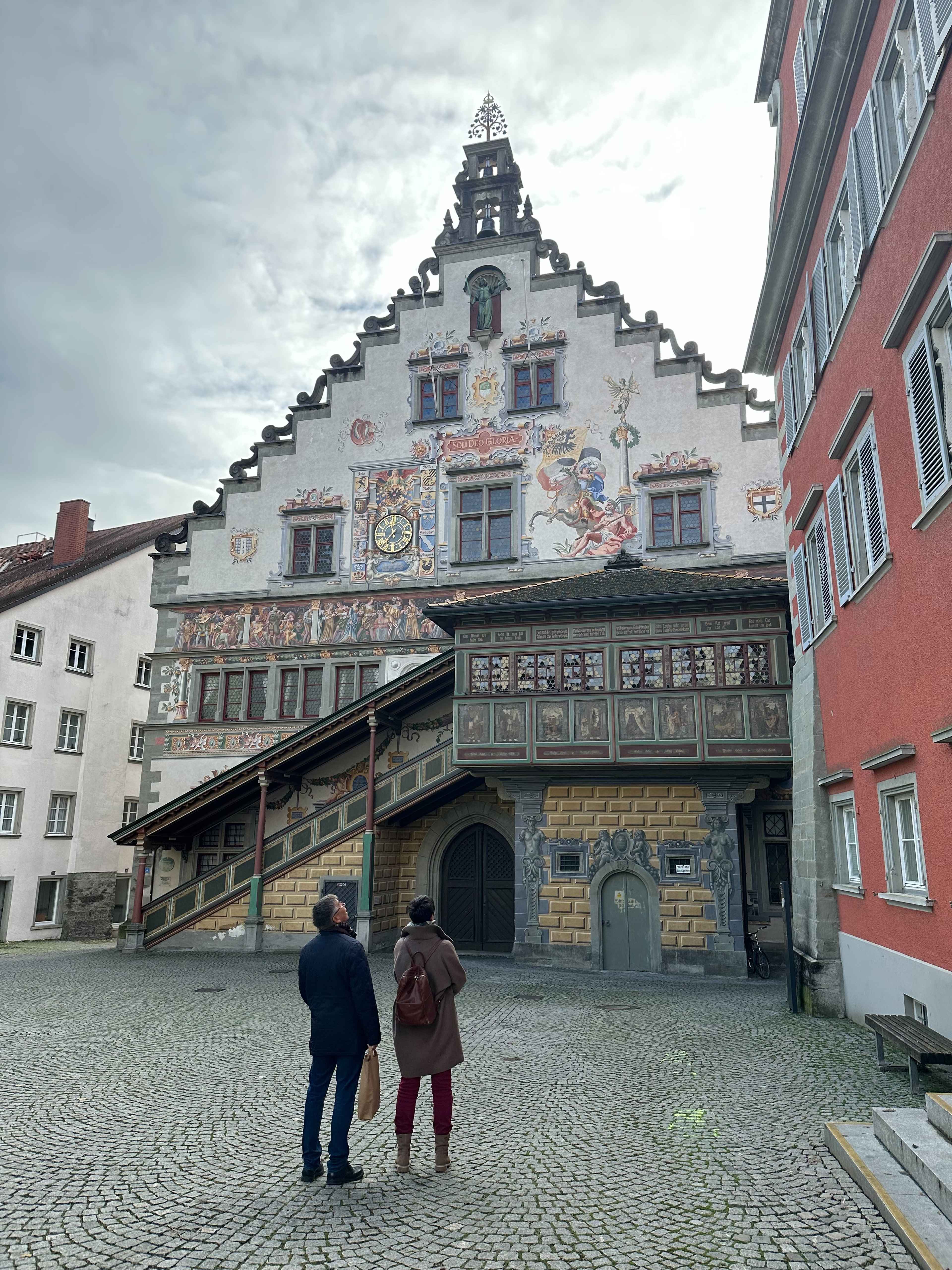 Historisches Rathaus in Lindau mit aufwendigen Wandmalereien und Figuren, darunter zwei Personen, die das Gebäude betrachten.
