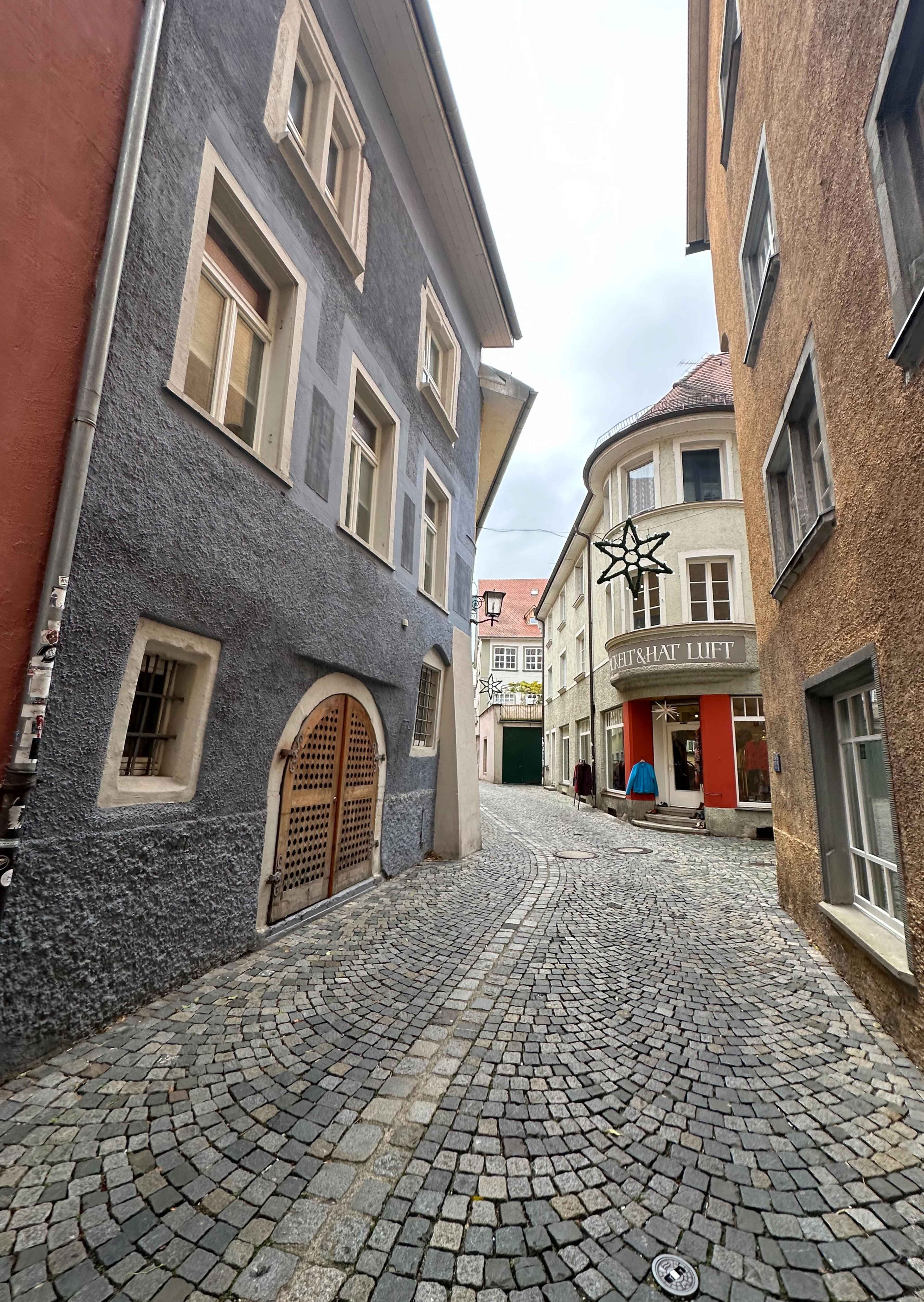 Schmale Kopfsteinpflasterstraße mit alten Häusern, dazwischen ein Stern als Deko. Links ein graues Gebäude mit Rundfenster.