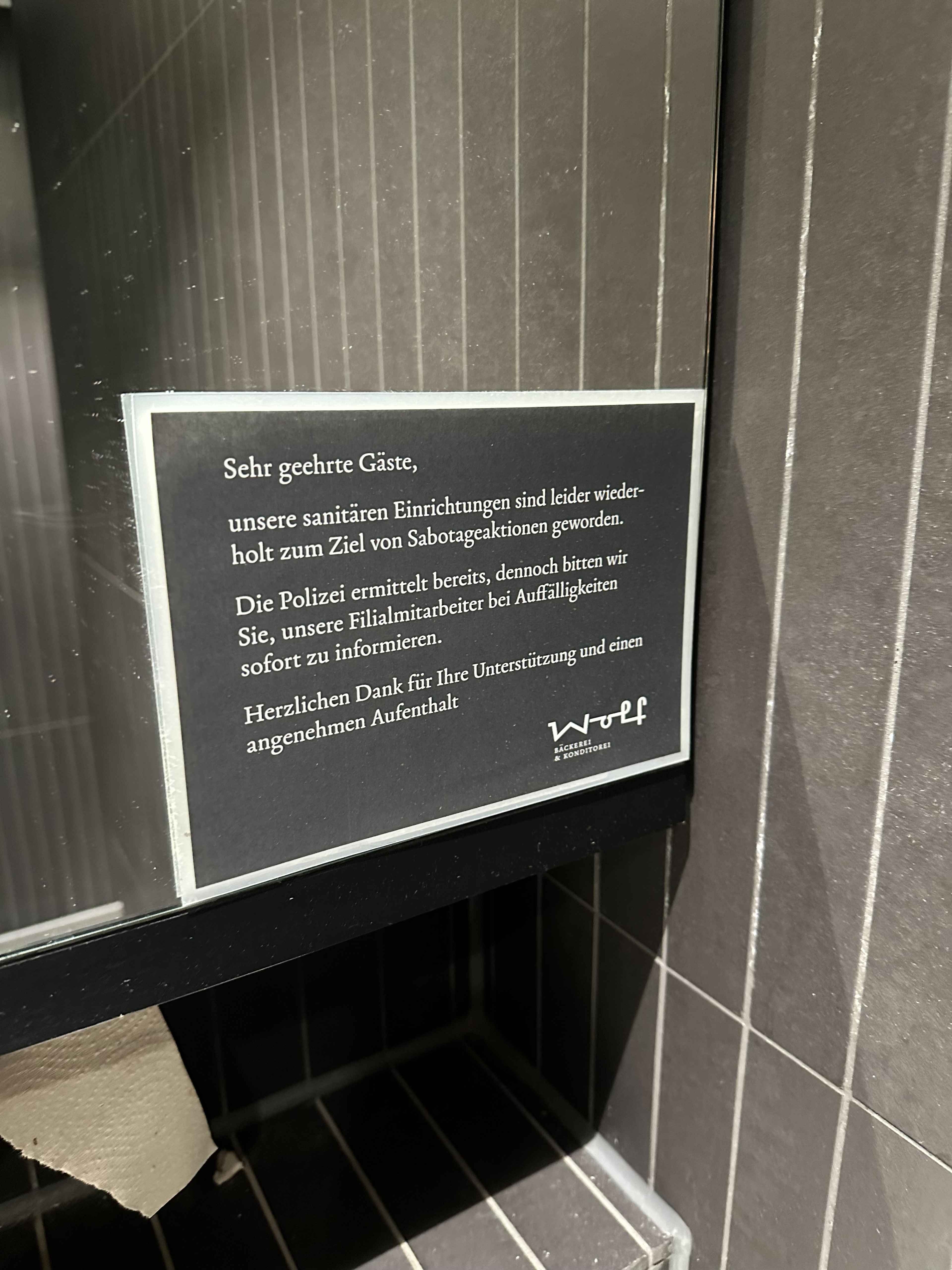 Hinweisschild in der Toilette eines Bäckers, das Gäste über Sabotageaktionen an sanitären Anlagen informiert.